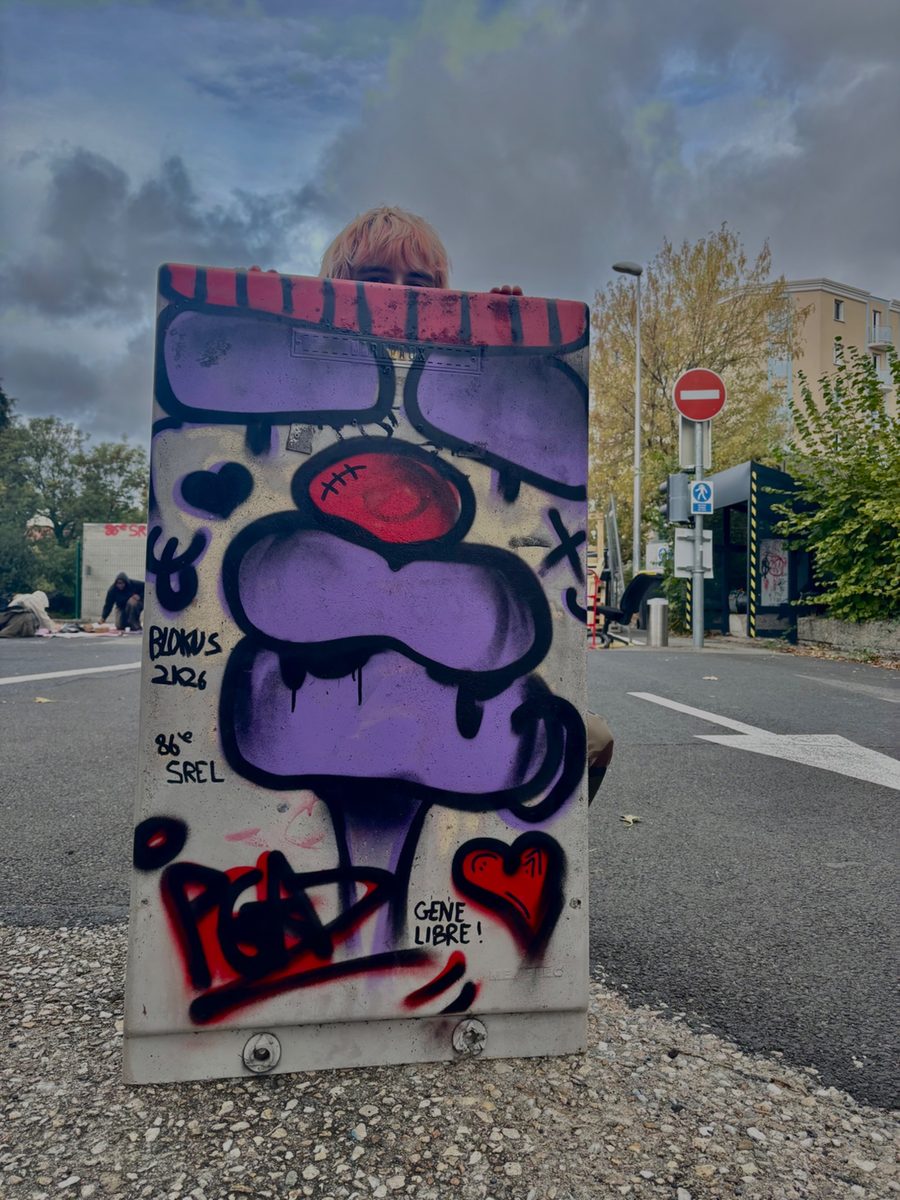 Armoire électrique recouverte d'un graffiti violet et rouge, avec les inscriptions « Blokus 2K26 » et « Gene libre ! »