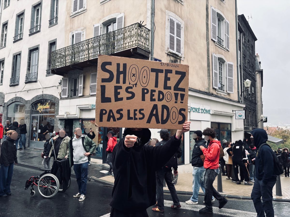 Manifestant au visage masqué brandissant une pancarte « Shootez les pédo !! Pas les ados » dans une rue du centre-ville