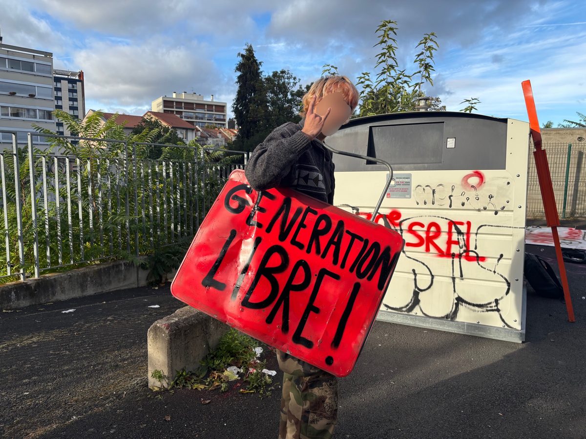 Personne portant sur l'épaule un panneau rouge « Génération libre ! » devant un conteneur tagué