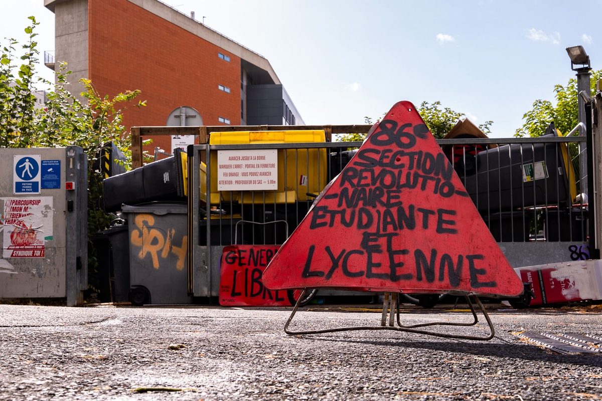 Panneau triangulaire rouge « 86e section révolutionnaire étudiante et lycéenne » posé devant une barricade de poubelles