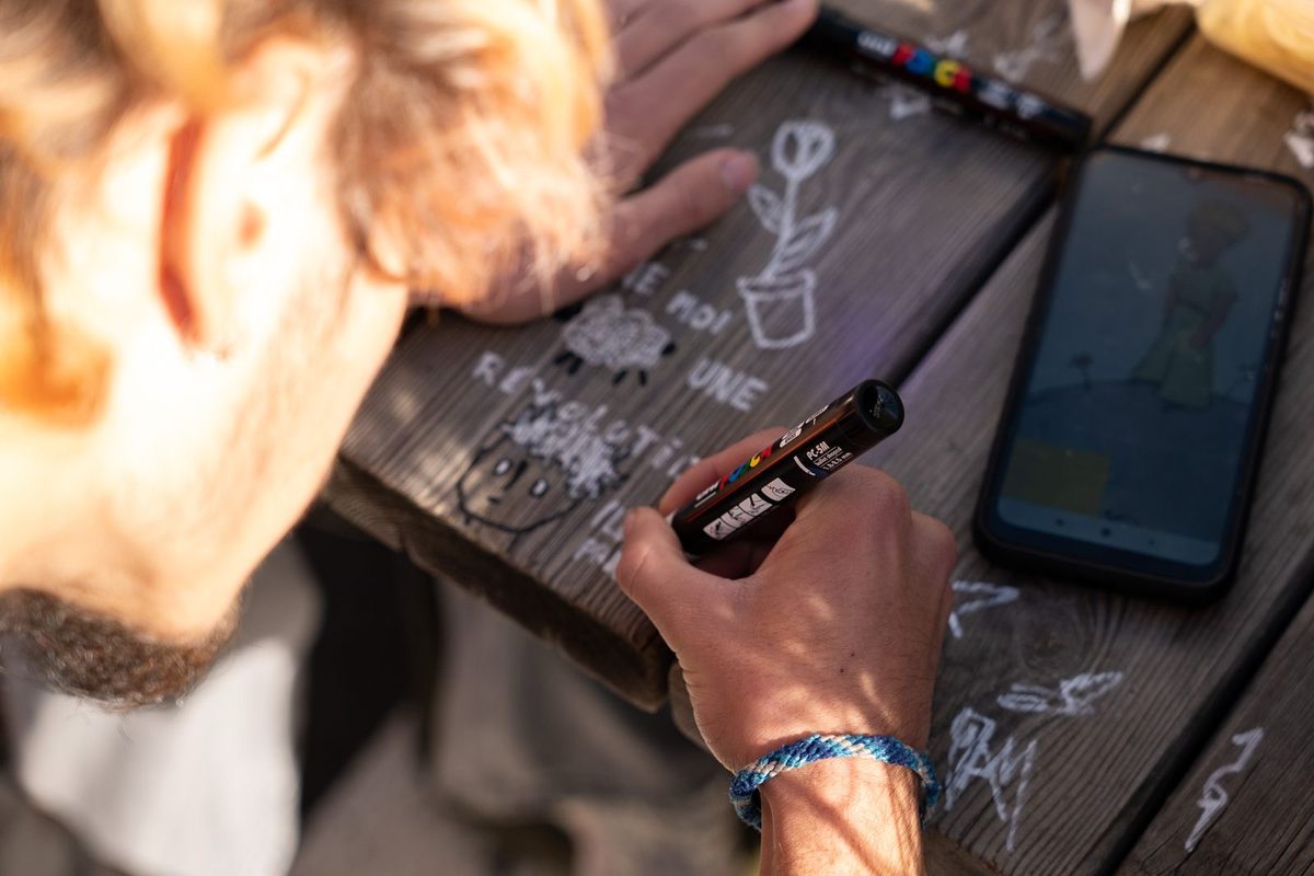 Vue de dessus d'une personne dessinant au Posca sur une table en bois, avec un mouton et une fleur dessinés