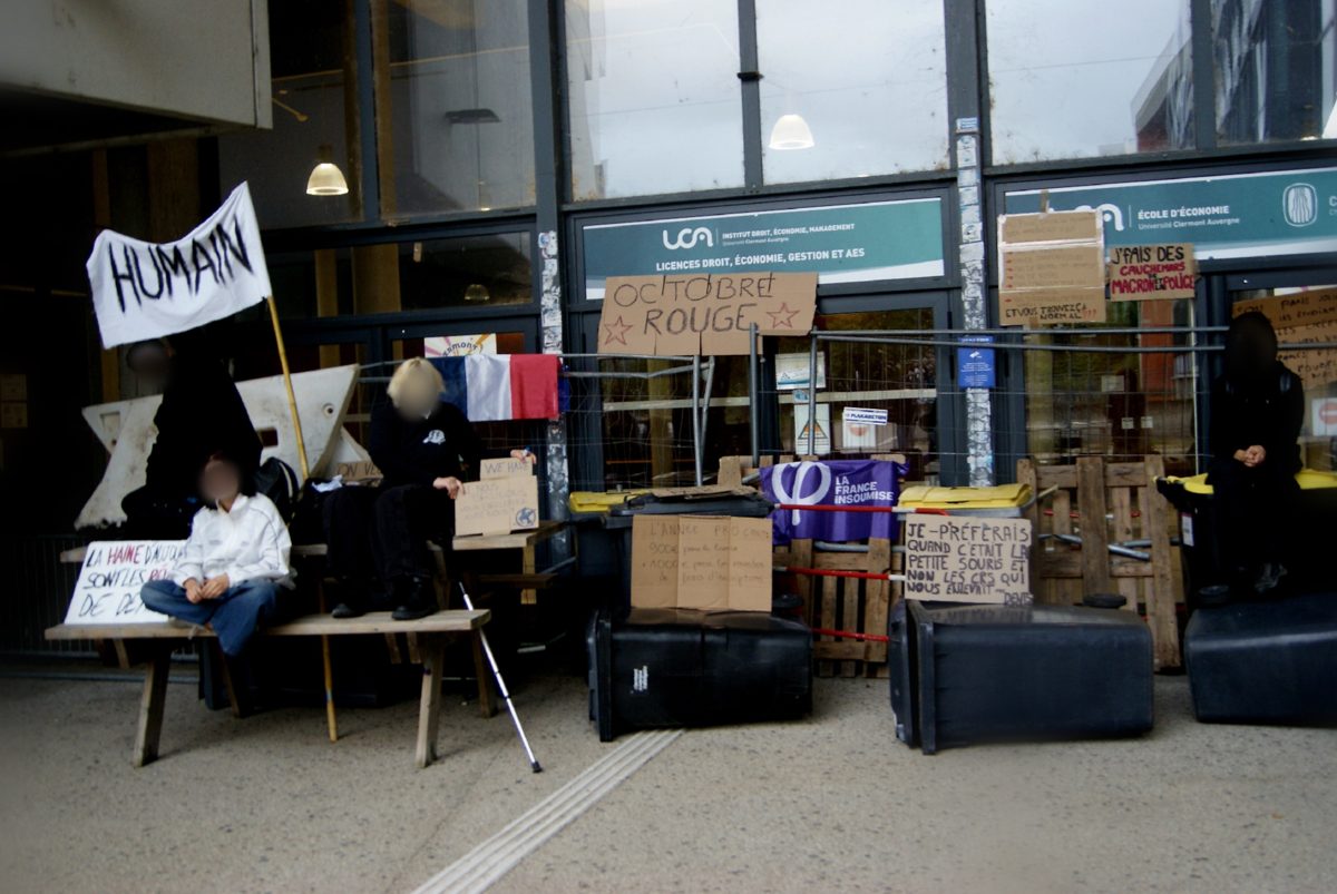 Barricade de poubelles et de palettes devant l'entrée d'un bâtiment, avec pancartes « Octobre rouge » et banderole « Humain »