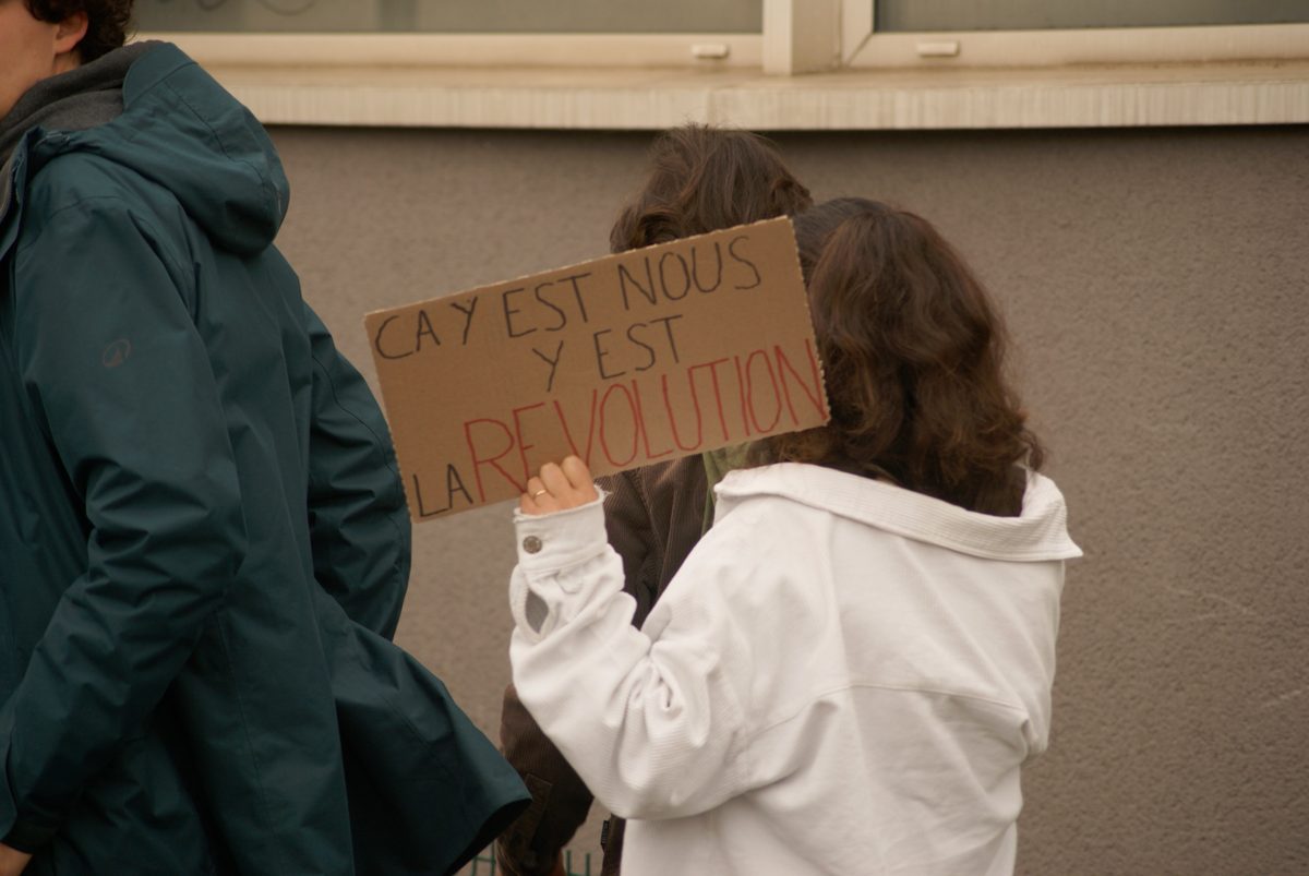 Personne de dos tenant une pancarte en carton : « Ça y est, nous y est la révolution »